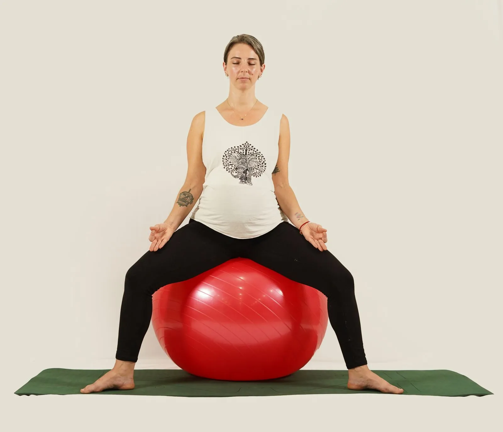 Pregnant woman sitting on a red exercise ball practicing meditation, featuring serene expression and yoga pose.